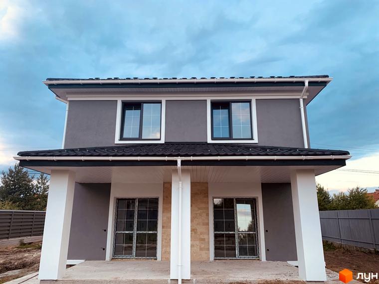 Двоповерховий будинок в Котеджному містечку Vita House з сірими стінами, білими колонами та вікнами. Навколо будинку видно будівельний майданчик.