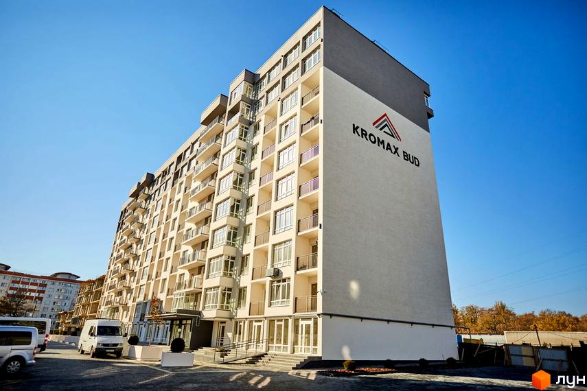 Зовнішній вигляд багатоповерхового будинку Житлового комплексу KromaxBud з великим логотипом на фасаді. На передньому плані припарковані автомобілі та облаштована територія.