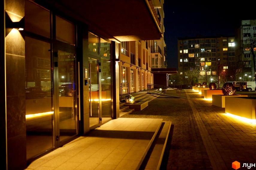 Вечірнє фото фасаду та прибудинкової території Житлового комплексу KromaxBud. Освітлення підкреслює архітектуру будівлі та ландшафтний дизайн.