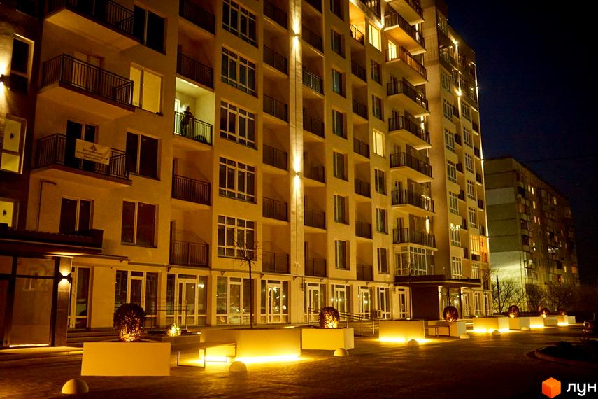 Новобудова ЖК KromaxBud вночі з підсвіченим фасадом та балконами. Прибудинкова територія з ландшафтним освітленням та зонами відпочинку.