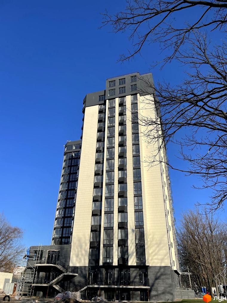 Житловий комплекс Park Plaza: високий будинок з бежевим фасадом, темними вікнами та цоколем. Навколо видно голі дерева та елементи будівництва.