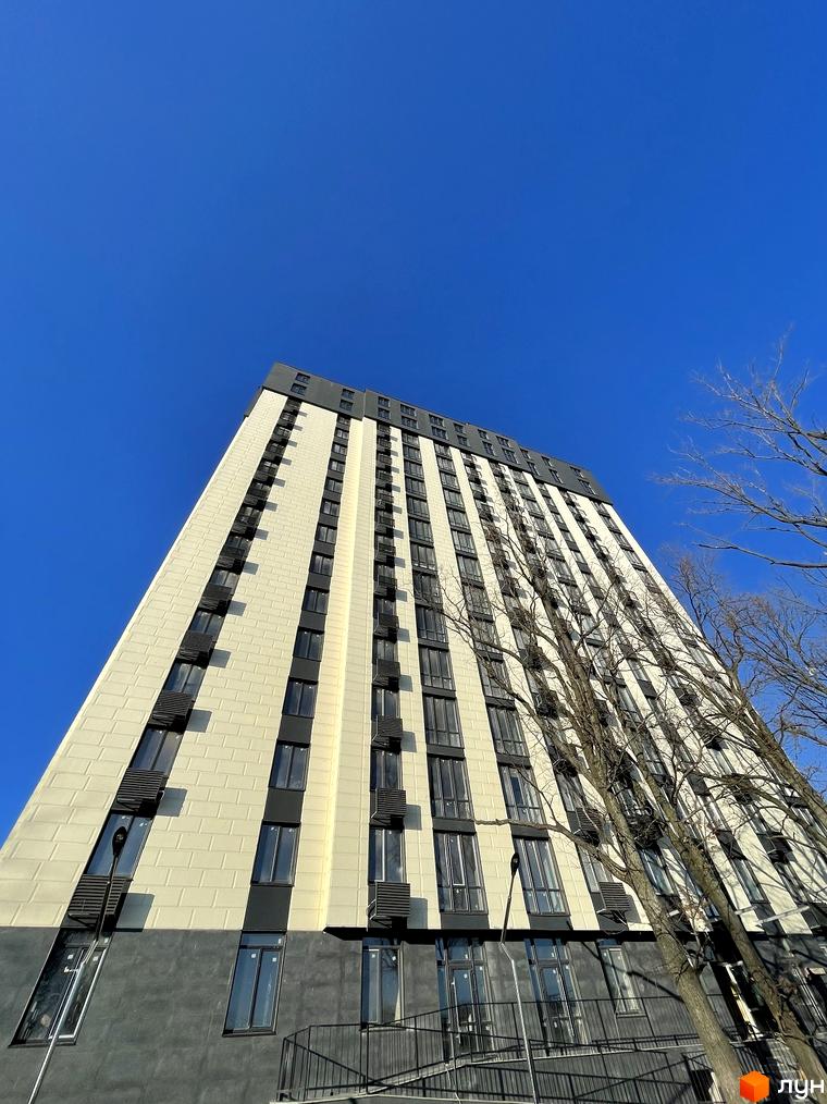 Висока новобудова Park Plaza з бежевим фасадом, темними вертикальними смугами та великими вікнами. Поруч розташовані голі дерева під блакитним небом.