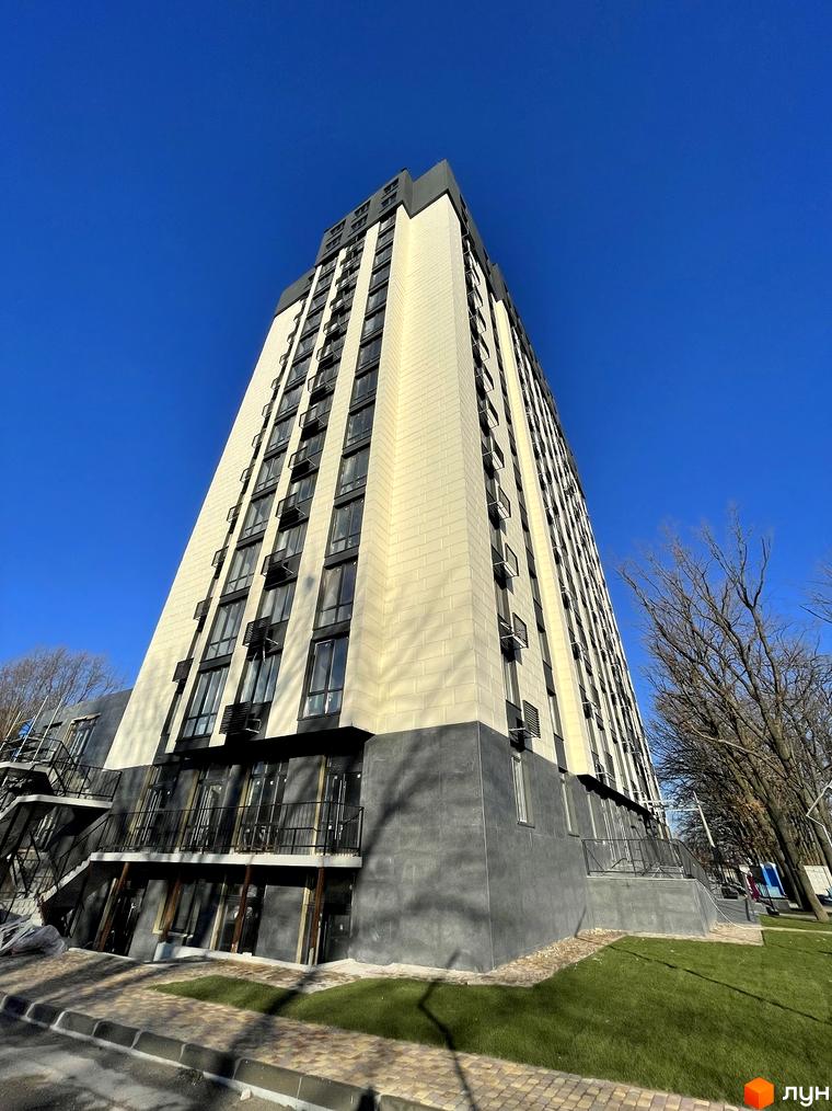 Житловий комплекс Park Plaza: висотна будівля з кремовим фасадом та темними вікнами. Навколо будинку зелені газони та дерева під блакитним небом.