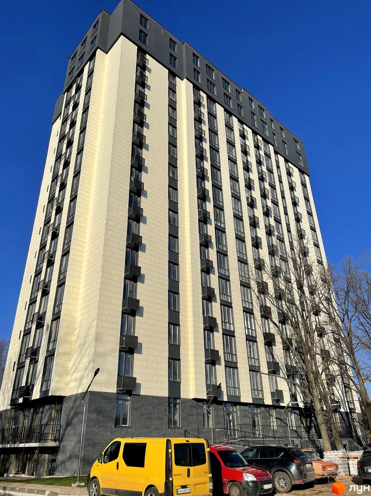 Житловий комплекс Park Plaza з бежевим фасадом та темними віконними рамами на тлі синього неба. Поруч припарковані автомобілі та дерева.