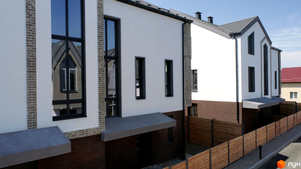 Котеджне містечко КМ New Smart 7. Зовнішній вигляд будинків з великими вікнами та цегляним оздобленням, огороджена територія з дерев'яним парканом.