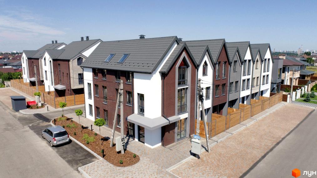 Котеджне містечко КМ New Smart 7. Зовнішній вигляд будинків з цегляним та білим фасадом, сірим дахом, огородженою територією та автомобілем на парковці.