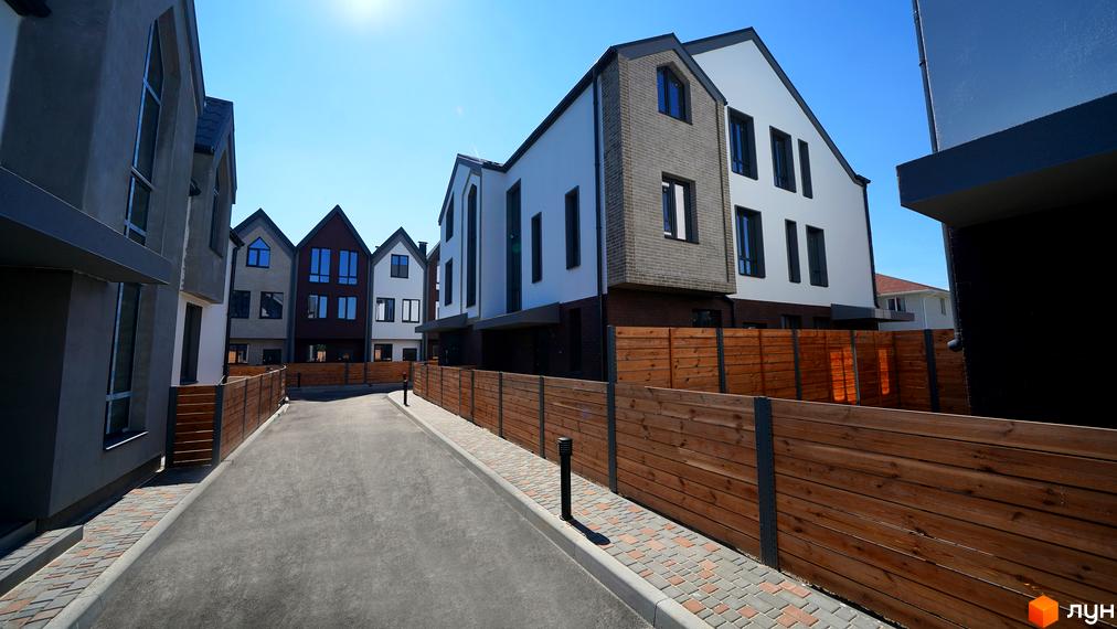 Котеджне містечко КМ New Smart 7: фасади будинків з цегли та штукатурки, дерев'яні паркани та доглянута прибудинкова територія.