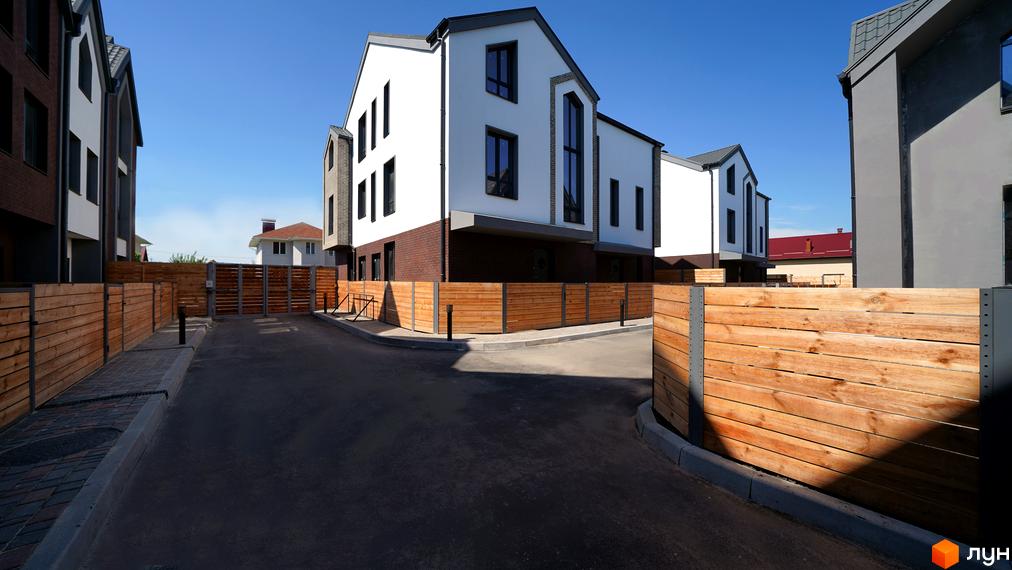 Котеджне містечко КМ New Smart 7. Зовнішній вигляд будинків з білою та цегляною обробкою, огороджених дерев'яним парканом.