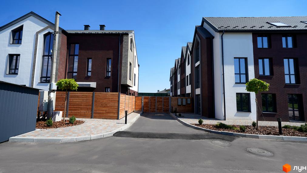 Котеджне містечко KМ New Smart 7. Зовнішній вигляд будинків з коричневої та білої цегли, з дерев'яними елементами, та прибудинкова територія з бруківкою та зеленими насадженнями.