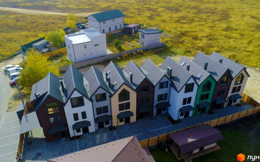 Зображення таунхаусів New Smart X з сірими дахами та різнокольоровими фасадами. Навколо будинків зелена територія та парковка.