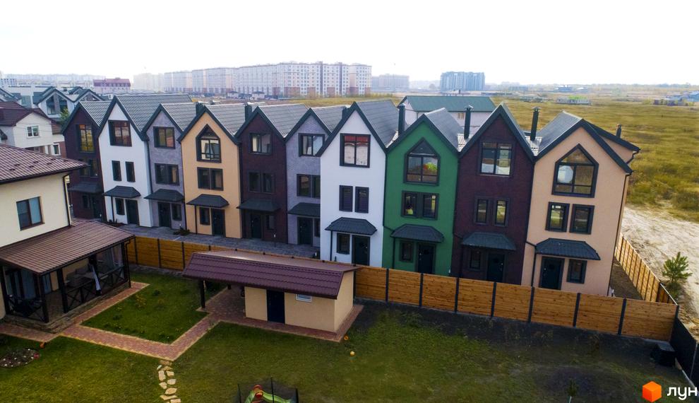 Фото таунхаусів New Smart X з різнокольоровими фасадами та великими вікнами. Навколо будинків зелений газон та дерев'яна огорожа.