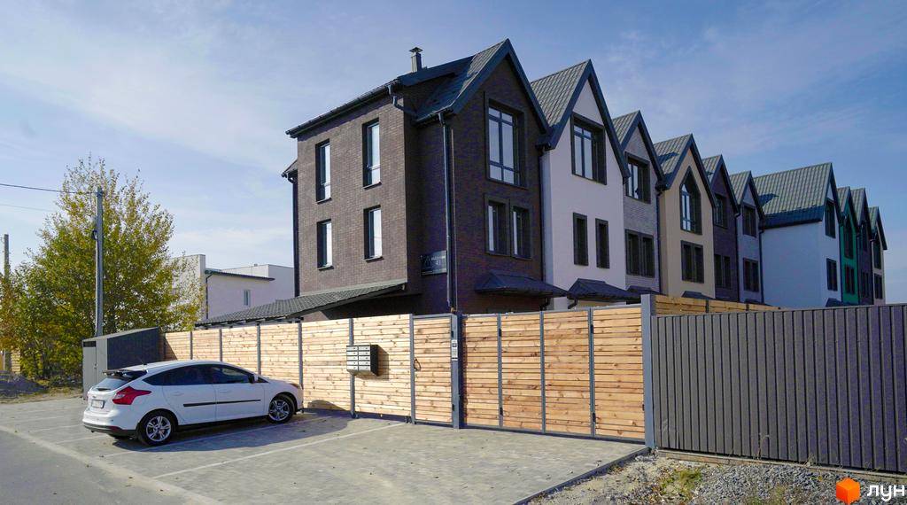 Зовнішній вигляд таунхаусів New Smart X з темною цеглою та сірими дахами. Перед будинками парковка та дерев'яна огорожа.