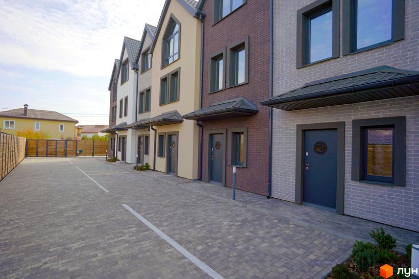 Зовнішній вигляд таунхаусів New Smart X з цегляними фасадами та сірими дверима. На передньому плані вимощена бруківкою територія.