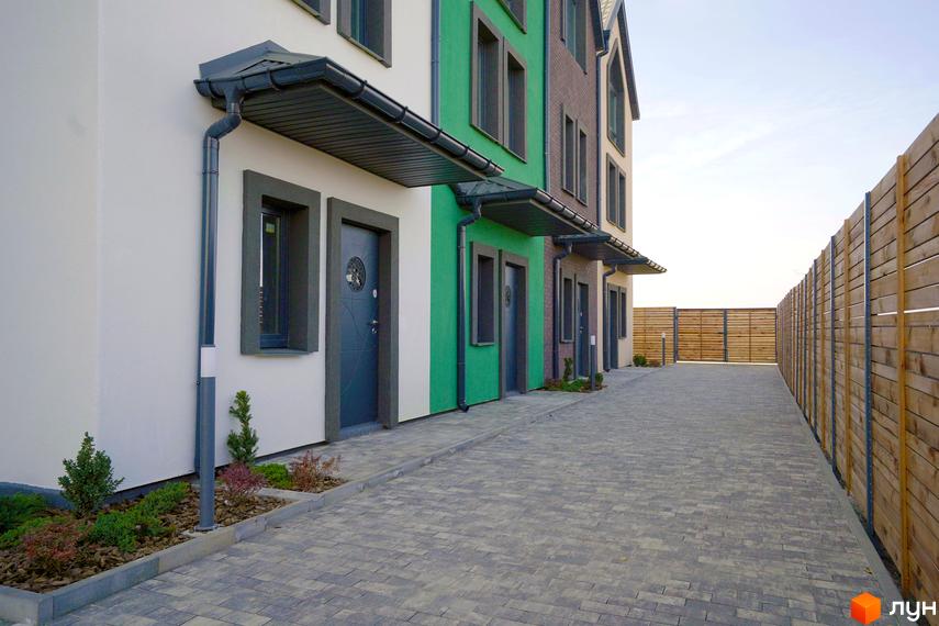 Фасад таунхаусів New Smart X з вхідними дверима та вікнами, вимощеною тротуарною плиткою дорогою та дерев'яним парканом.