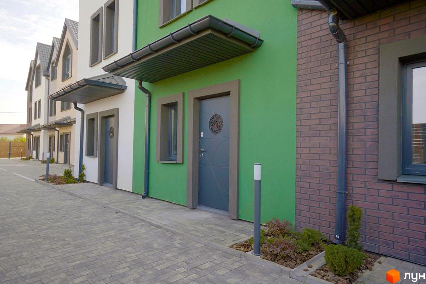 Зовнішній вигляд таунхаусів New Smart X з різнокольоровими фасадами та тротуарною плиткою на прибудинковій території.