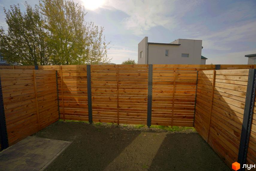 Вид на дерев'яний паркан та прибудинкову територію Житлового комплексу New Smart X. На задньому плані видно будинок.
