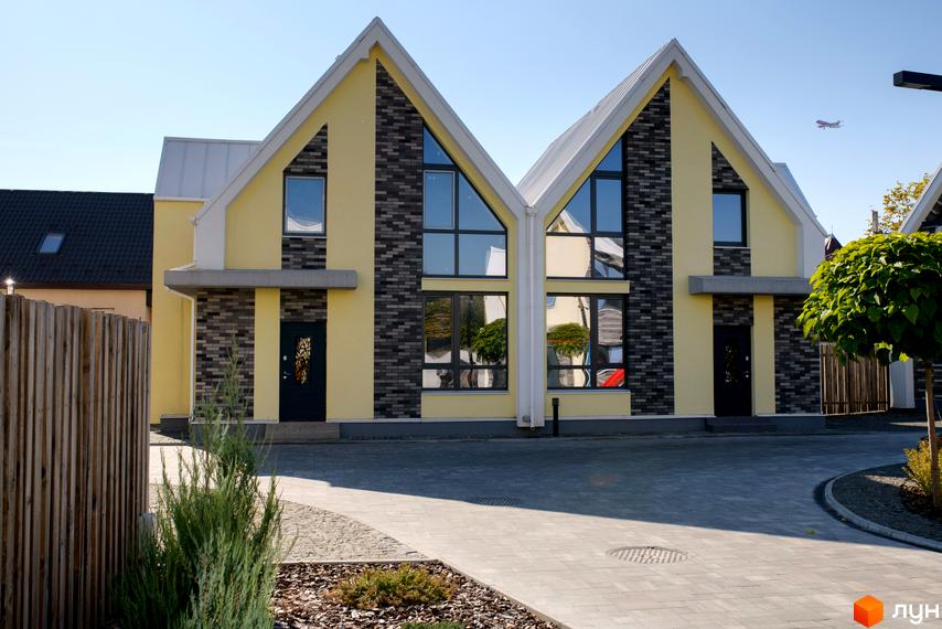 Два котеджі Котеджного містечка Solo Home з жовтими фасадами, темною цеглою та великими вікнами. Прибудинкова територія вимощена бруківкою з елементами озеленення.