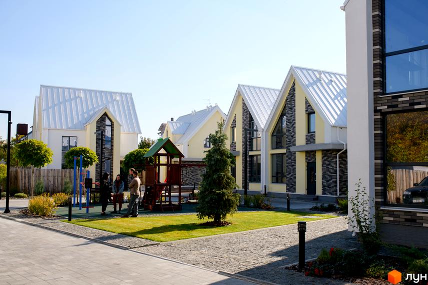 Котеджне містечко Solo Home: будинки зі світло-жовтими фасадами, білими дахами та темними цегляними вставками. На території є дитячий майданчик та зелені газони.