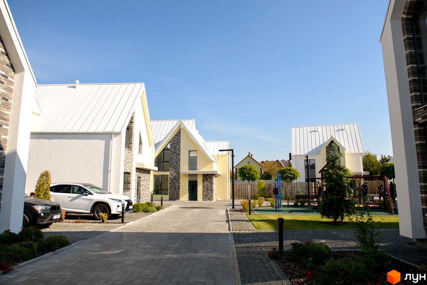 Котеджне містечко Solo Home: будинки зі світлими фасадами та білими дахами, бруковані доріжки та дитячий майданчик.