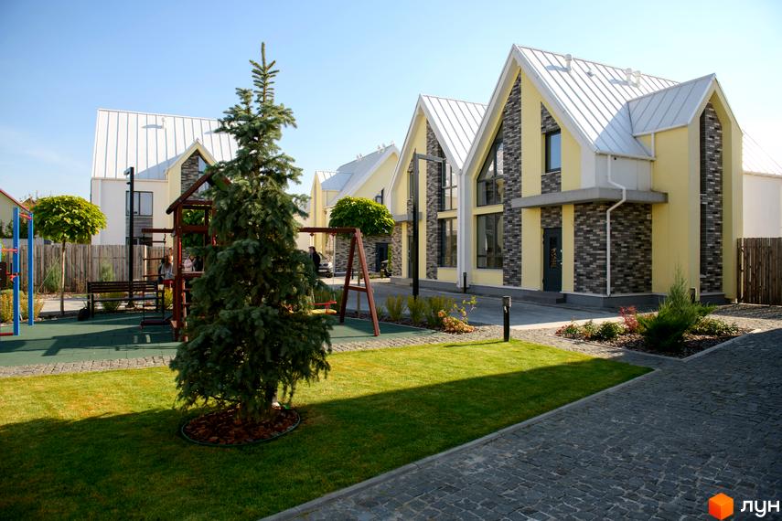 Котеджне містечко Solo Home: світло-жовті будинки з білими дахами та цегляними вставками, поруч зелений газон та дитячий майданчик.