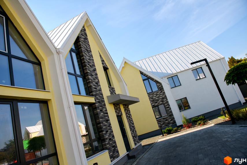 Котеджне містечко Solo Home: будинки з високими дахами, жовтими та цегляними фасадами, великими вікнами. Територія з бруківкою та озелененням.