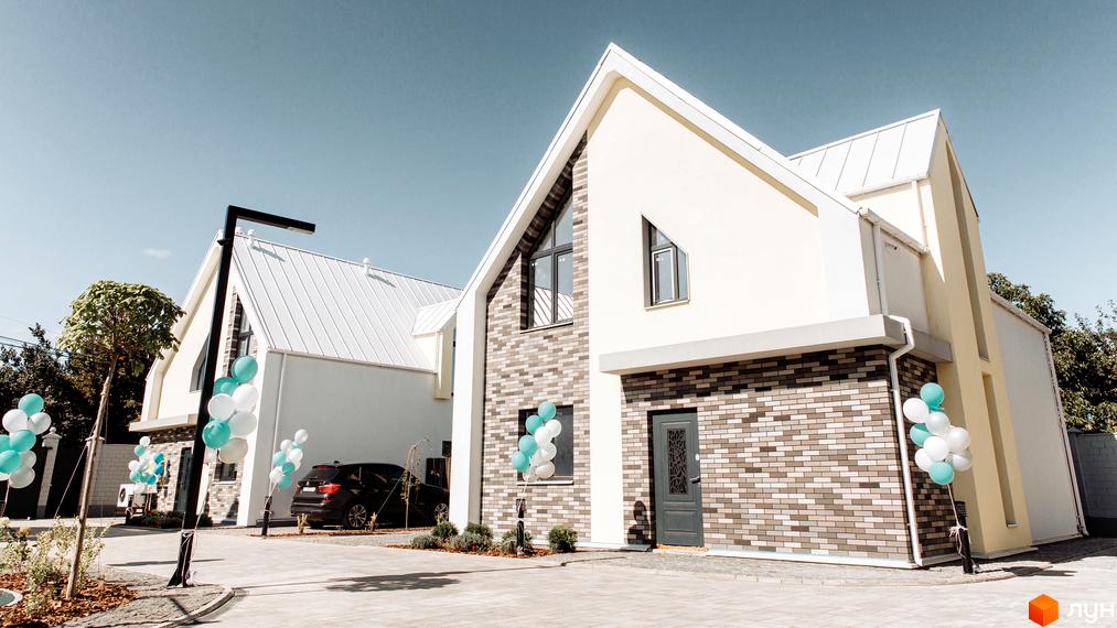 Будинок Котеджного містечка Solo Home зі світлим фасадом, цегляною кладкою та білим дахом, з бруківкою та деревами на подвір'ї.