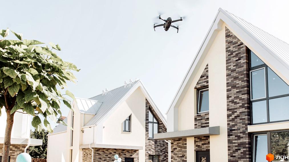 Будинки Котеджного містечка Solo Home з білими дахами та цегляними фасадами. Над ними літає дрон, поруч росте дерево.
