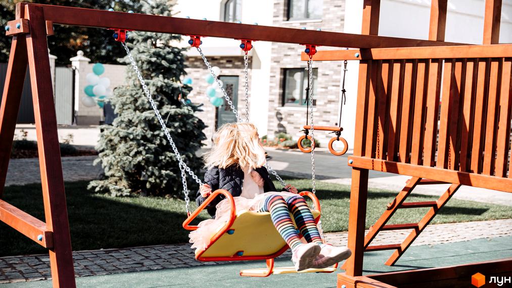 Будинок Котеджного містечка Solo Home має світлий цегляний фасад. На прибудинковій території розташований дитячий майданчик з гойдалками та зелений газон.