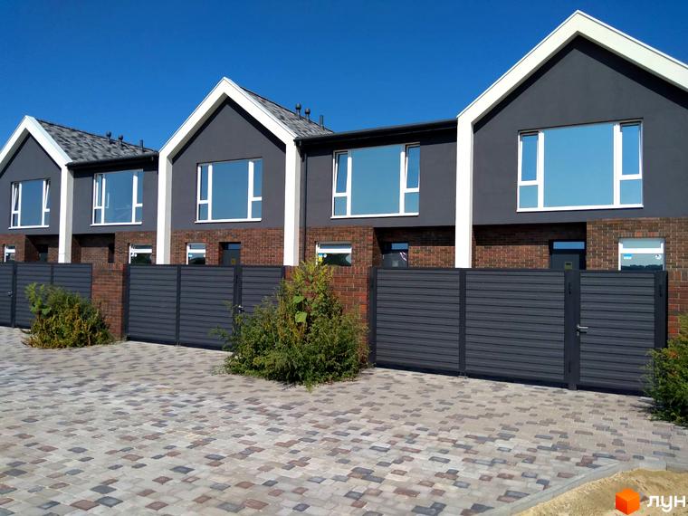 Зовнішній вигляд таунхаусів Town Park з сірими стінами, великими вікнами та огорожею. На передньому плані викладена бруківкою прибудинкова територія.