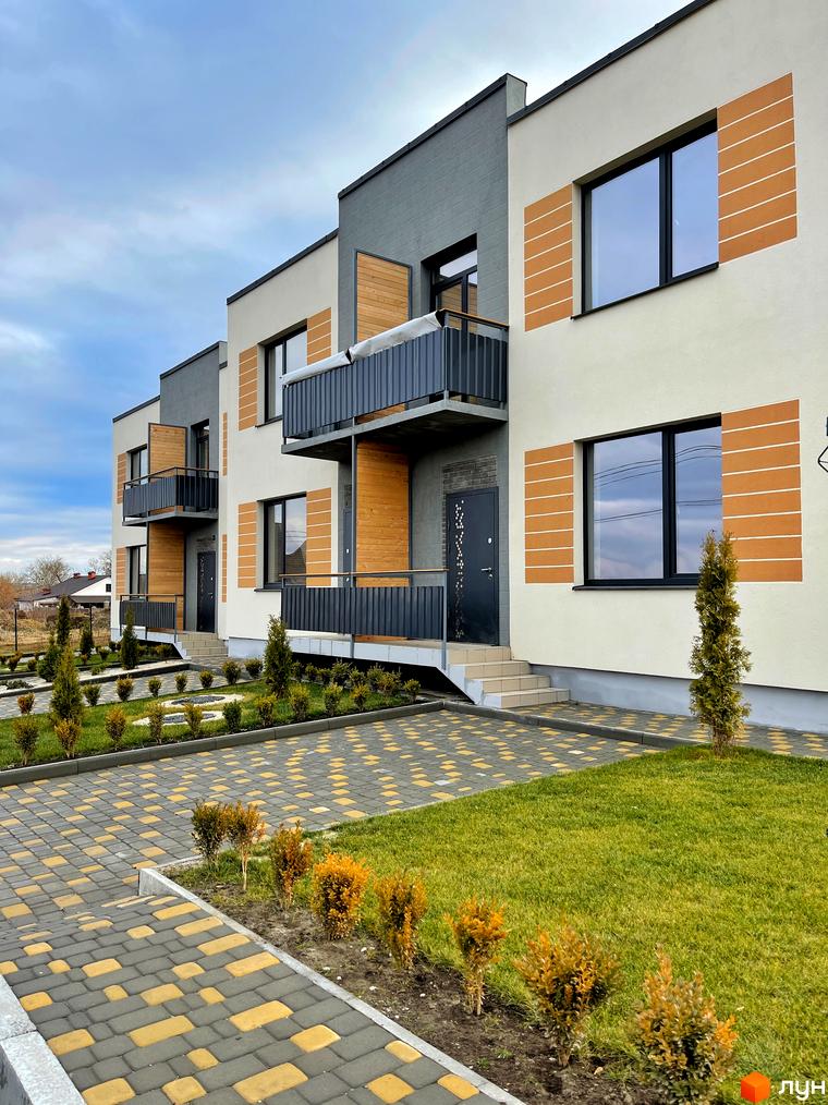 Зовнішній вигляд таунхаусів Twin House з білими фасадами, чорними вікнами та балконами. Прибудинкова територія з газонами, тротуарами з бруківки та декоративними кущами.