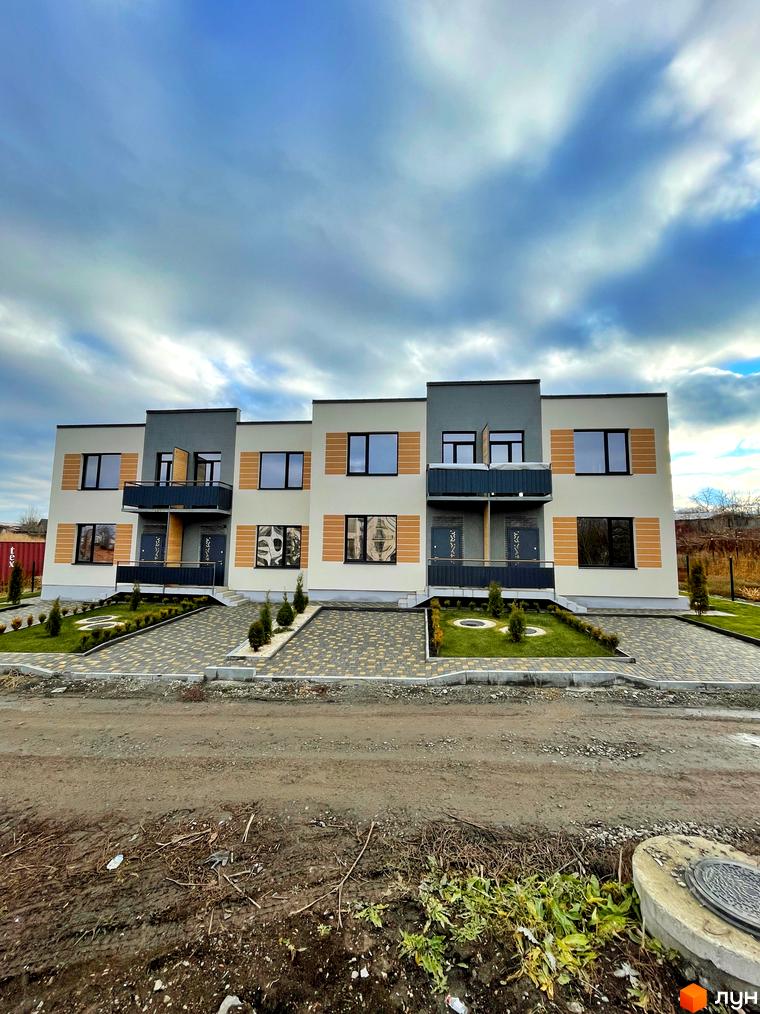 Триповерхові таунхауси Twin House з темними балконами та вікнами, фасади світлого кольору з дерев'яними вставками. Перед будинками бруківка та газон з туями.