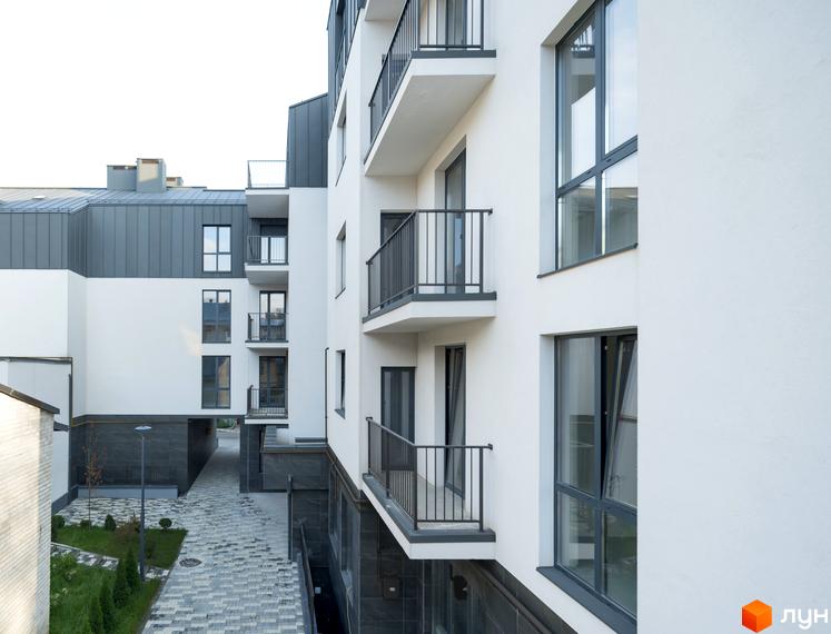 Новобудова ЖК Globus Elite з білими фасадами, балконами та темними вікнами. Прибудинкова територія з доріжками та зеленими насадженнями.