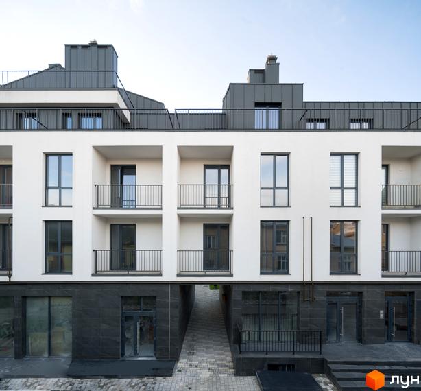 Зовнішній вигляд новобудови ЖК Globus Elite з білими фасадами, балконами та темними вікнами. Навколо будинку бруківка та вхідна група.