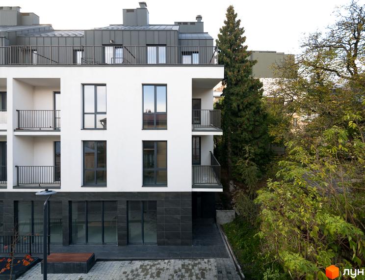 Фасад житлового комплексу Globus Elite з балконами та великими вікнами. Поруч розташована прибудинкова територія з лавкою та ліхтарем.