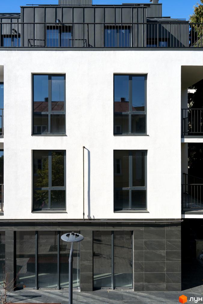 Фасад новобудови ЖК Globus Elite з білими стінами та темними вікнами. На першому поверсі розташовані великі вітринні вікна з чорною плиткою.