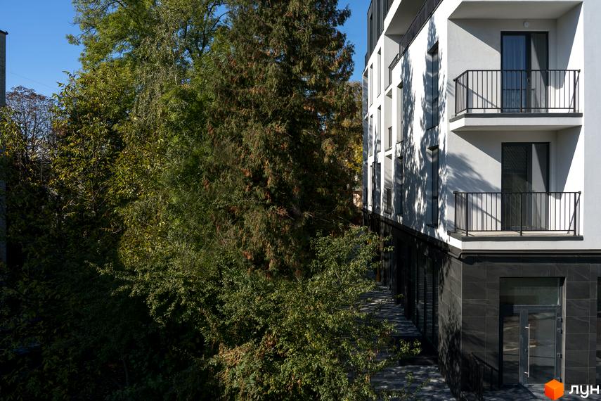 Новобудова ЖК Globus Elite з балконами та вікнами, оточена деревами. Зовнішній вигляд будівлі та зелена прибудинкова територія.