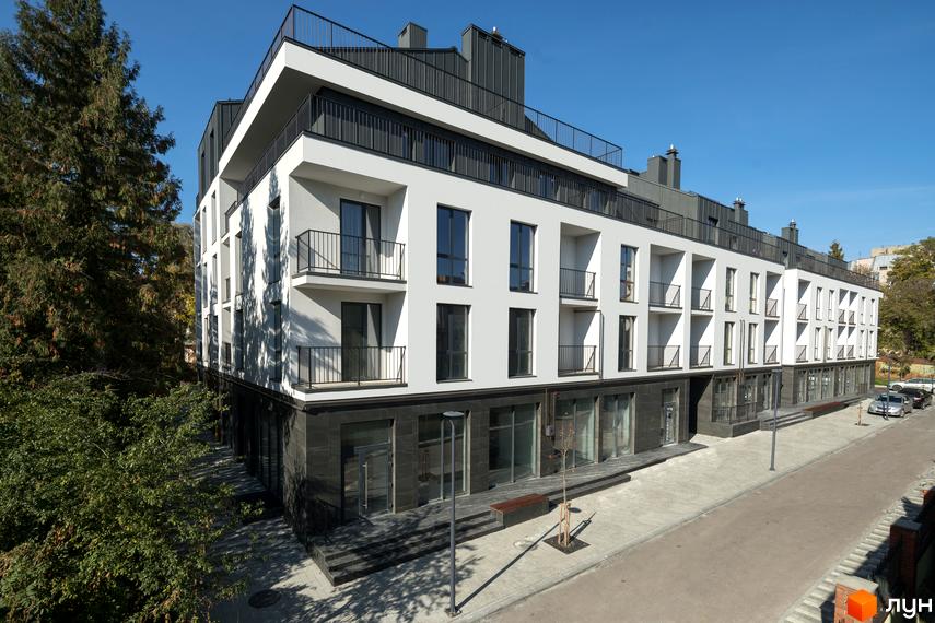 Будинок ЖК Globus Elite з білими фасадами, темними балконами та великими вікнами. Поруч розташована доглянута прибудинкова територія з деревами та тротуаром.