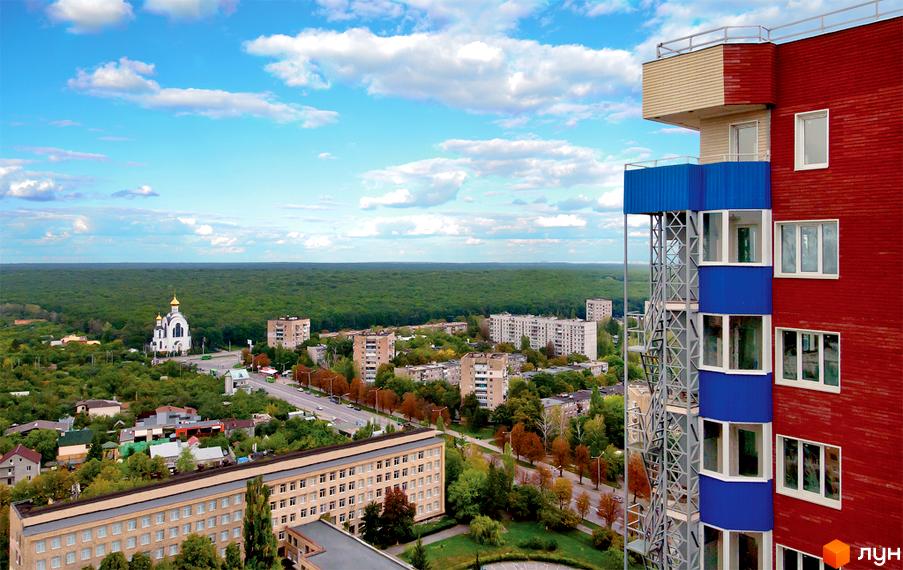 Житловий комплекс Монте-Плаза з червоно-синім фасадом та білими вікнами. Панорамний вид на міський пейзаж, церкву та ліс.