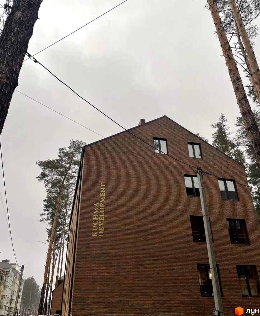 Зображення фасаду цегляного будинку з великими вікнами та написом KUCHMA DEVELOPMENT. Навколо будівлі ростуть високі дерева.