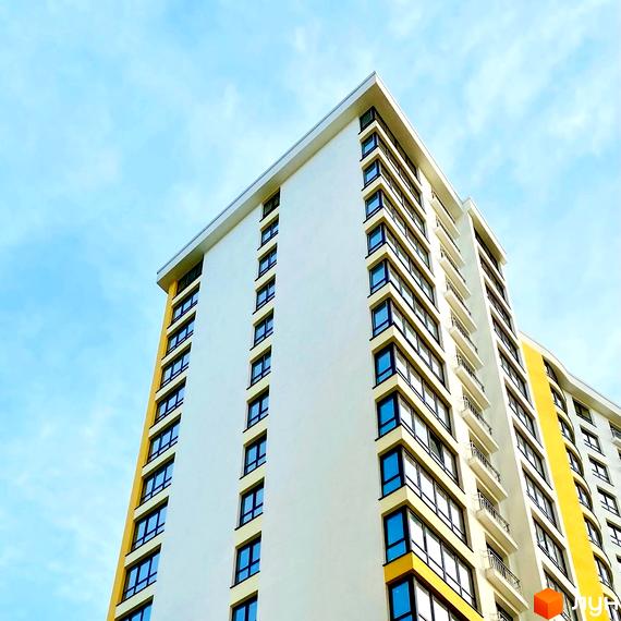 Сучасний житловий комплекс Lystopad з біло-жовтим фасадом та численними вікнами під блакитним небом. Зовнішній вигляд будівлі вражає своєю акуратністю та геометричністю.