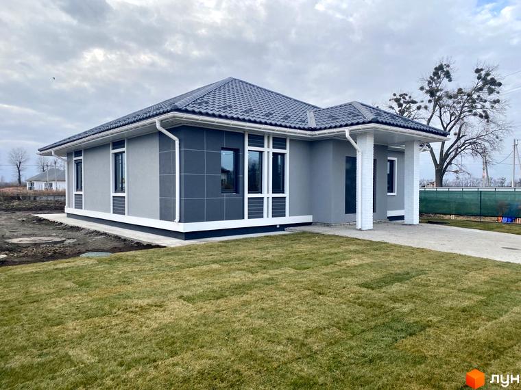 Одноповерховий будинок з сірими стінами та темним дахом. Перед будинком газон, поруч асфальтована доріжка. КМ Крушинка Парк.