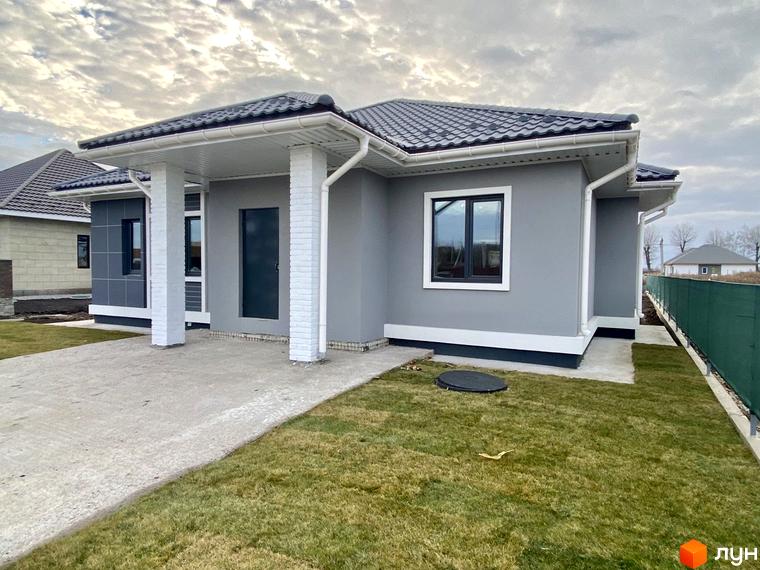 Котеджне містечко Крушинка Парк: одноповерховий будинок сірого кольору з білими колонами та темним дахом. Навколо доглянутий газон та бетонна доріжка.