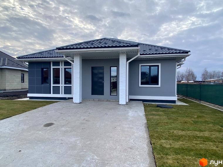 Одноповерховий будинок в Містечку котеджів Крушинка Парк з сірим фасадом та бетонною доріжкою. Поряд газон та зелений паркан.