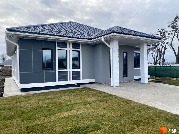 Одноповерховий будинок в Котеджному містечку Крушинка Парк з темним дахом та фасадом, білими колонами та доглянутим газоном.