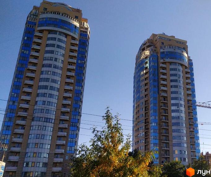 Житловий комплекс Аквамарин - висотні будинки з блакитними та бежевими фасадами, балконами та панорамними вікнами на тлі блакитного неба.