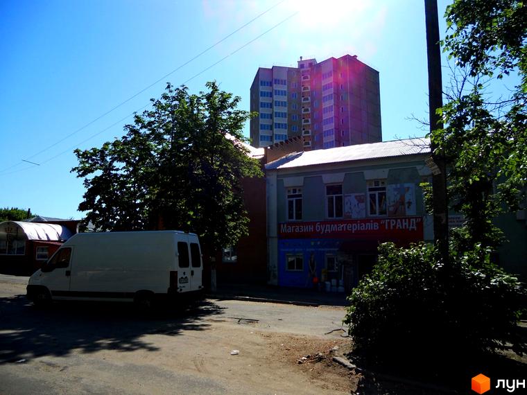 Зовнішній вигляд житлового комплексу на вул. Першого Травня, 12/1. Прибудинкова територія з зеленими насадженнями та автомобілем.