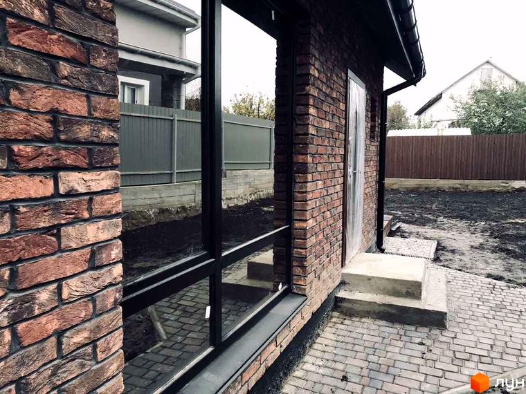 Котеджне містечко Одноповерховий Київ - Дніпро: фасад будинку з темно-червоної цегли, великими вікнами та чорною водостічною системою. Прибудинкова територія з бруківкою.