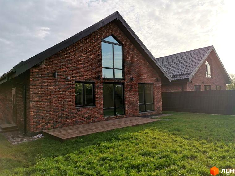 Котеджне містечко КМ Одноповерховий Київ - Дніпро. Зовнішній вигляд будинку з червоної цегли та дерев'яна тераса на фоні зеленої галявини.