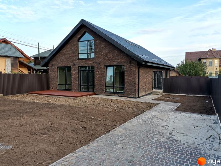 Котеджне містечко КМ Одноповерховий Київ - Дніпро: цегляний будинок з великими вікнами та терасою на тлі зеленого двору та паркану.