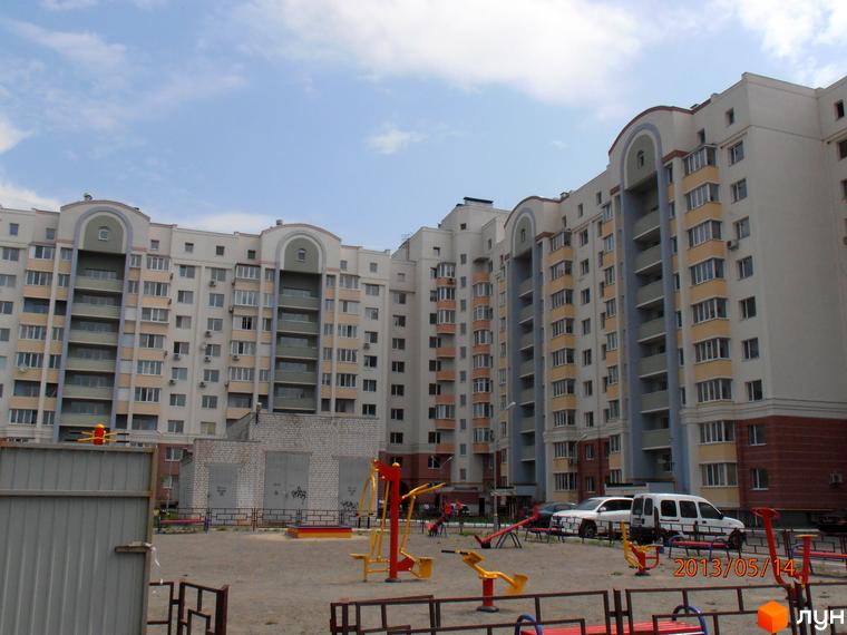 Житловий комплекс Юність з фасадом та балконами, прибудинкова територія з дитячим майданчиком та автомобілями.